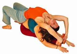 Auf den Rücken legen und die Füße zum Kopf ziehen. Für die Helfende eine gute Flexibilitätsübung für die Brustwirbelsäule.