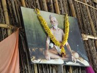 Fotografierte, mit einer Girlande geschmückte Porträtdarstellung Ramana Maharshis.